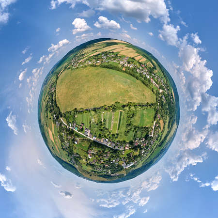 Aerial view from high altitude of little planet earth with small village houses and distant green cultivated agricultural fields with growing cropsの写真素材