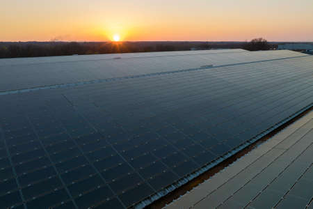 Aerial view of solar power plant with blue photovoltaic panels mounted on industrial building roof for producing green ecological electricity. Production of sustainable energy conceptの写真素材