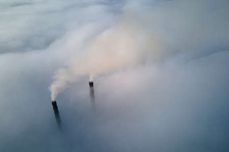 Coal power plant high pipes emitting black poisonous smoke moving upwards over white fog polluting air. Production of electrical energy with fossil fuel conceptの写真素材
