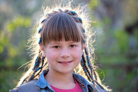 Portrait of happy smiling young teen girl in casual clothes with blue ribbons in long braids...
