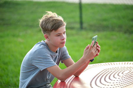 Young handsome teenager boy using smartphone outdoors on sunny summer day. Technology generation conceptの写真素材