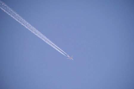 Distant passenger jet plane flying on high altitude on clear blue sky leaving white smoke trace of contrail behind. Air transportation conceptの写真素材