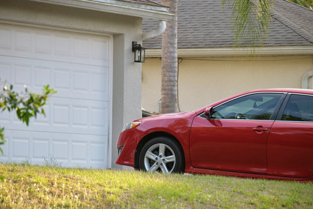 Car parked in front of wide garage double door on concrete driveway of new modern american houseの写真素材