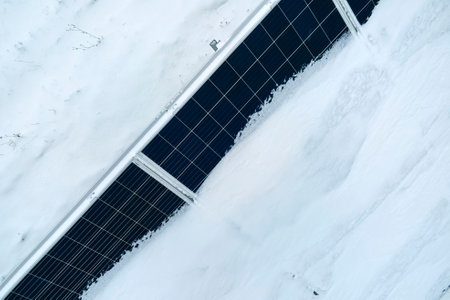 Aerial view of snow covered sustainable electric power plant with rows of solar photovoltaic panels...