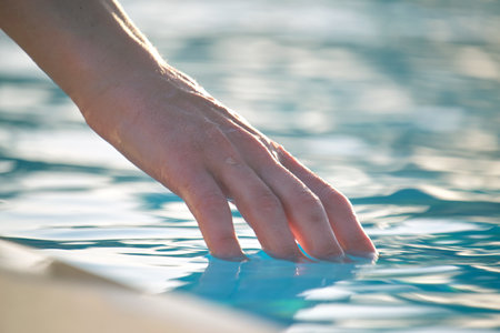 Female hand touching water of swimming pool in summerの写真素材