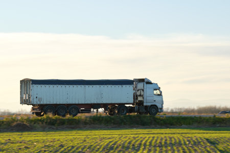 Semi-truck with tipping cargo trailer transporting sand from quarry driving on highway hauling goods in evening. Delivery transportation and logistics conceptの写真素材