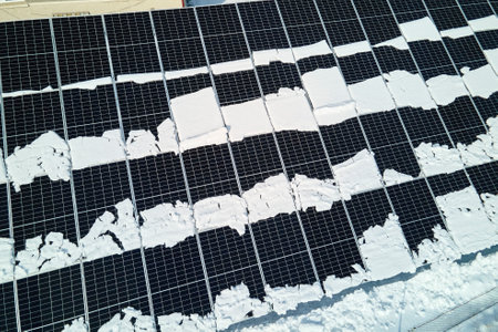 Aerial view of electrical power plant with solar panels covered with snow melting down in winter end...
