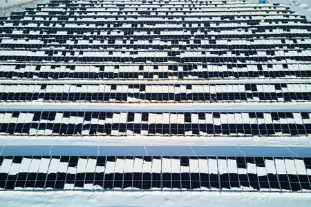 Aerial view of electrical power plant with solar panels covered with snow melting down in winter end...