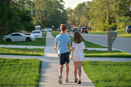 Rear view of two young teenage children, girl and boy, brother and sister walking together on rural...
