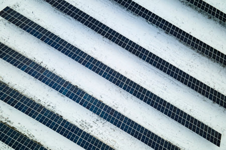 Aerial view of electrical power plant with solar panels covered with snow melting down in winter end...