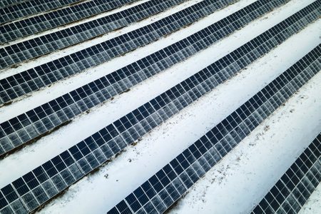 Aerial view of snow covered sustainable electric power plant with rows of solar photovoltaic panels for producing clean electrical energy. Low effectivity of renewable electricity in northern winterの写真素材