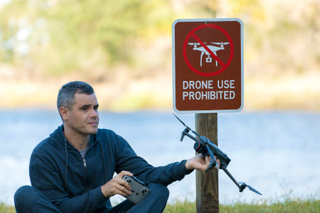 Drone operator is disappointed because he isnt allowed to fly his quadcopter in national park no drone area. Man is unable to use his UAV near restriction notice sign. Airspace use regulationsの写真素材