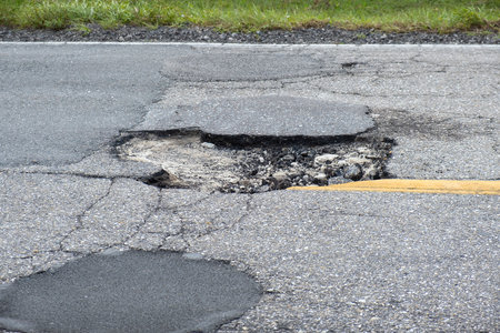 Damaged asphalt road with deep pothole on american highway surface. Ruined roadway in urgent need of repairの写真素材