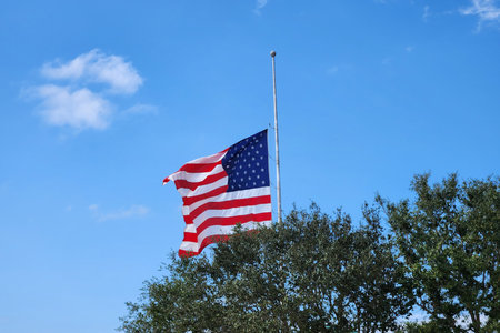 USA national flag waving lowered to half mast on wind against blue sky. American stars and stripes...