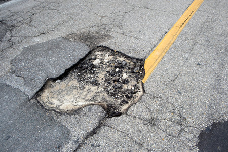 Damaged american road surface with deep pothole. Ruined street in urgent need of repairの写真素材