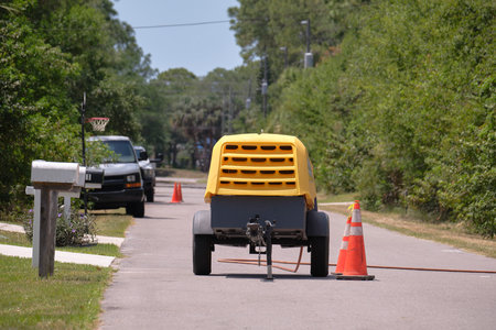 Yellow jackhammer machine with compressor trailer on road construction site