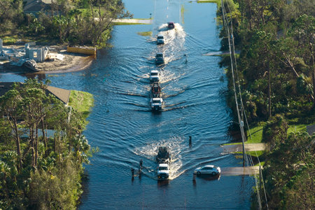 Flooded american street with moving vehicles and surrounded with water houses in Florida residential area. Consequences of hurricane natural disasterの写真素材