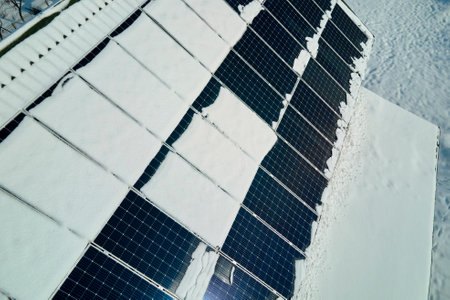 Aerial view of house roof with solar panels covered with snow melting down in winter end for...