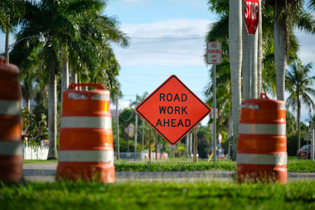 Road work ahead sign and barrier cones on street site as warning to cars about construction and utility worksの写真素材
