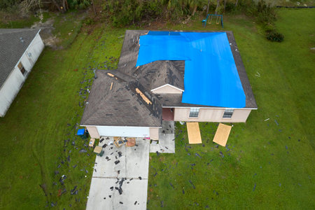Aerial view of damaged in hurricane Ian house roof covered with blue protective tarp against rain...