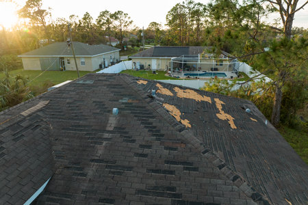 Wind damaged house roof with missing asphalt shingles after hurricane Ian in Florida. Repair of home...