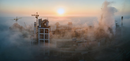 Aerial view of cement factory with high concrete plant structure and tower crane at industrial manufacturing site on foggy evening. Production and global industry conceptの写真素材