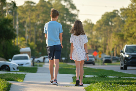 Rear view of two young teenage children, girl and boy, brother and sister walking together on rural street on bright sunny day. Vacation time conceptの写真素材