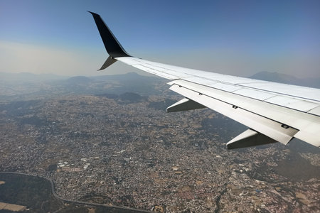 View through airplane window of commercial jet plane wing flying high in the sky ove big city. Air...