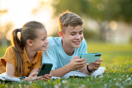 Happy children playing video games on their cellphones in summer park.