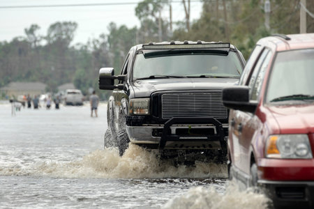 Flooded Florida road with evacuating cars and surrounded with water houses in suburban residential area. Consequences of hurricane natural disasterの写真素材