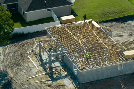 Professional builders working on roof construction of unfinished suburban home with wooden frame...