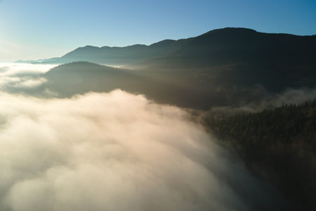Aerial view of colorful sunrise over white dense fog with distant dark silhouettes of mountain hills...