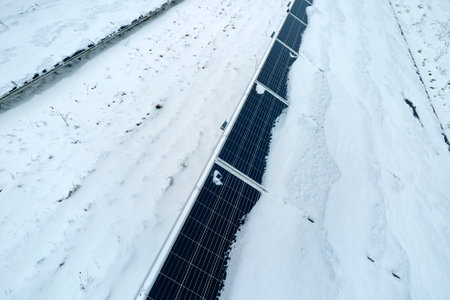Aerial view of snow covered sustainable electric power plant with rows of solar photovoltaic panels...