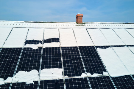 Aerial view of snow melting from covered solar photovoltaic panels installed on house rooftop for...