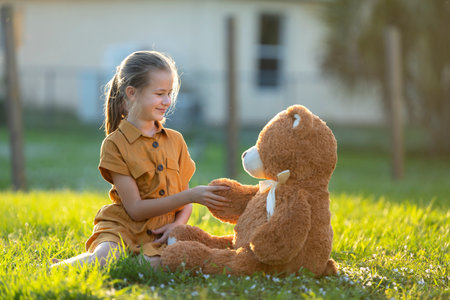 Friendly child girl shaking paw of her new teddy bear friend outdoors on green grass lawn. Friendship conceptの写真素材