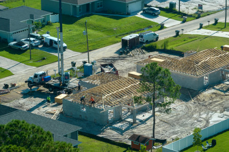 Lifting crane truck and builders working on roof construction of unfinished residential house with...