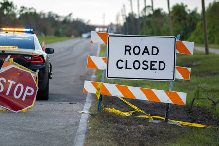 Police patrol car at warning roadworks sign and safety barrier on city street during maintenance...