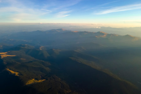Aerial view of dark mountain hills with bright sunrays of setting sun at sunset. Hazy peaks and misty valleys in eveningの写真素材