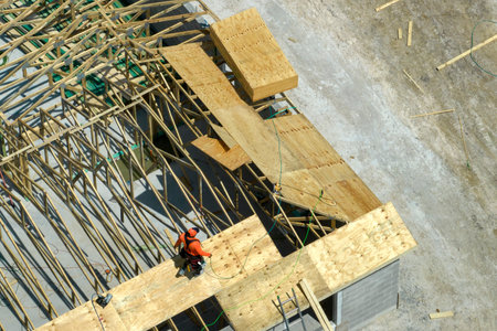 Professional builders working on roof construction of unfinished suburban home with wooden frame...
