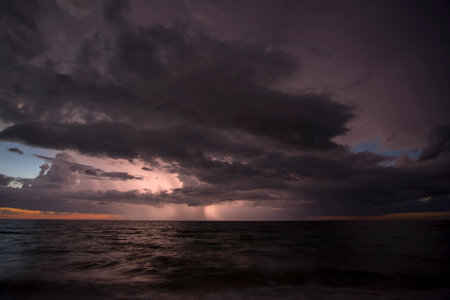 Thunderstorm dark clouds with lightning and thunder over evening sea water waves crushing on sandy...