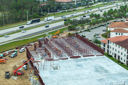 Industrial construction site with workers assembling metal frame building. Development of...