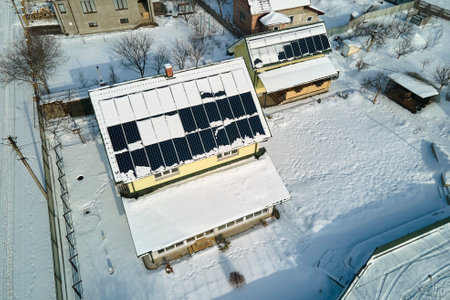 Aerial view of snow melting from covered solar photovoltaic panels installed on house rooftop for...