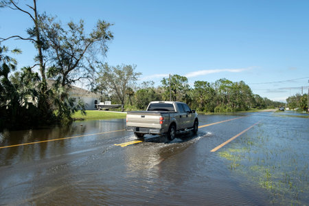 Flooded american street with moving vehicles and surrounded with water houses in Florida residential area. Consequences of hurricane natural disasterの写真素材