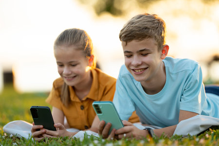 Positive children messaging on their mobile phones with friends outdoors in summer park.の写真素材