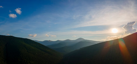 Aerial view of dark mountain hills with bright sunrays of setting sun at sunset. Hazy peaks and misty valleys in eveningの写真素材