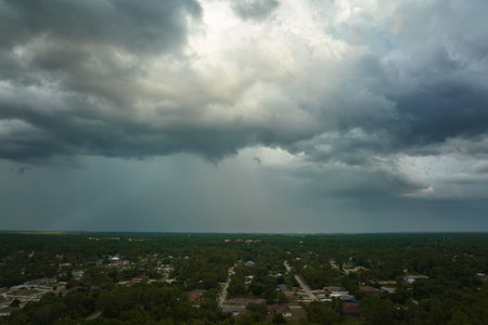 Dark stormy clouds forming on gloomy sky before heavy rainfall over suburban town areaの写真素材