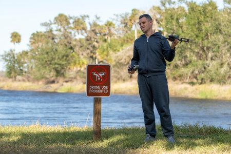 Drone operator is disappointed because he isnt allowed to fly his quadcopter in national park no drone area. Man is unable to use his UAV near restriction notice sign. Airspace use regulationsの写真素材