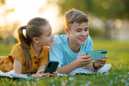 Positive children boy and girl playing online games on their mobile phones with friends outdoors in summer park.の写真素材