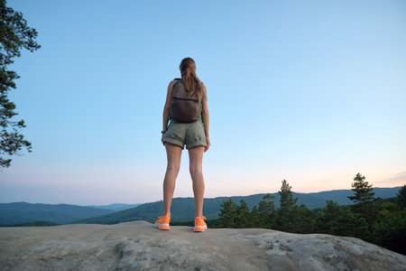 Young woman hiking alone on mountain footpath. Female hiker enjoying view of evening nature on wilderness trail. Active way of life conceptの写真素材