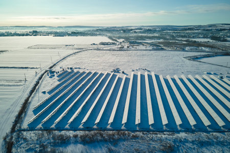 Aerial view of snow covered sustainable electric power plant with rows of solar photovoltaic panels for producing clean electrical energy. Low effectivity of renewable electricity in northern winterの写真素材